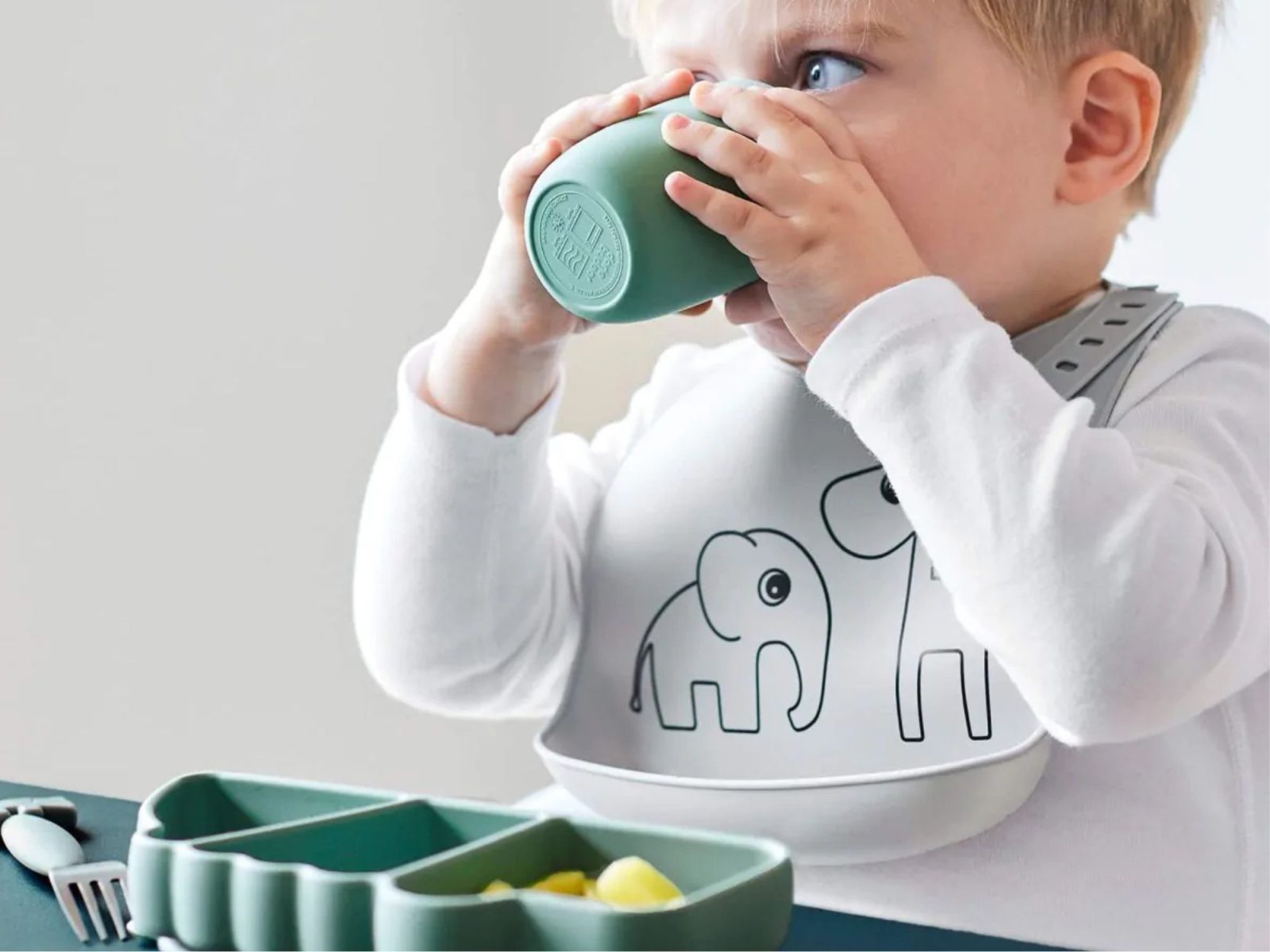 Jeune enfant utilisant une assiette compartimentée verte en silicone Done by Deer avec un bavoir éléphant