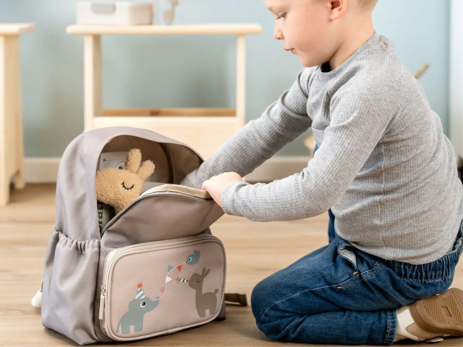 Enfant ouvrant un sac à dos sable Done by Deer illustré d’animaux festifs, idéal pour la maternelle