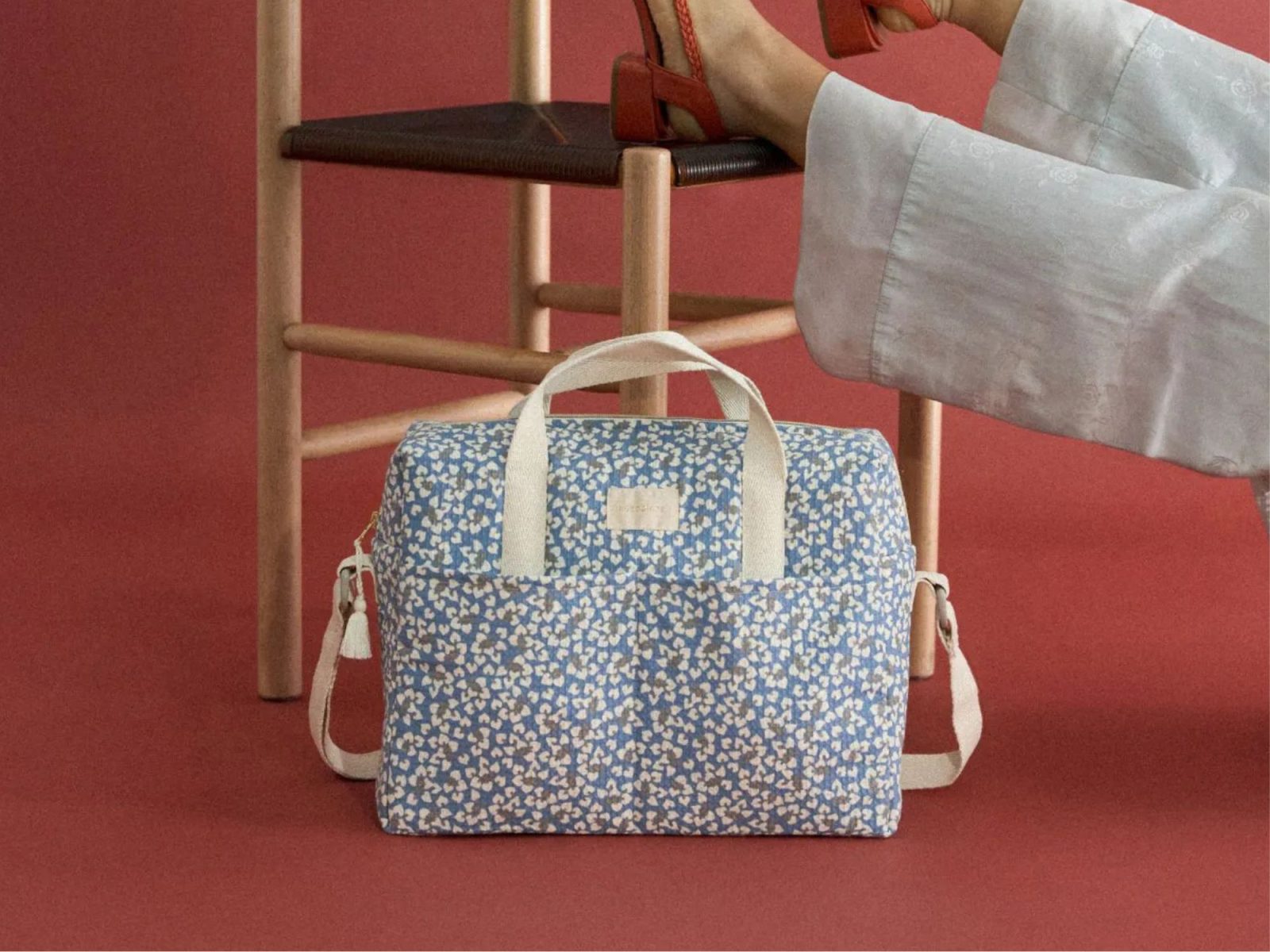 Sac à langer Nobodinoz Blue Yumiko à imprimé bleu fleuri posé au sol devant une chaise en bois