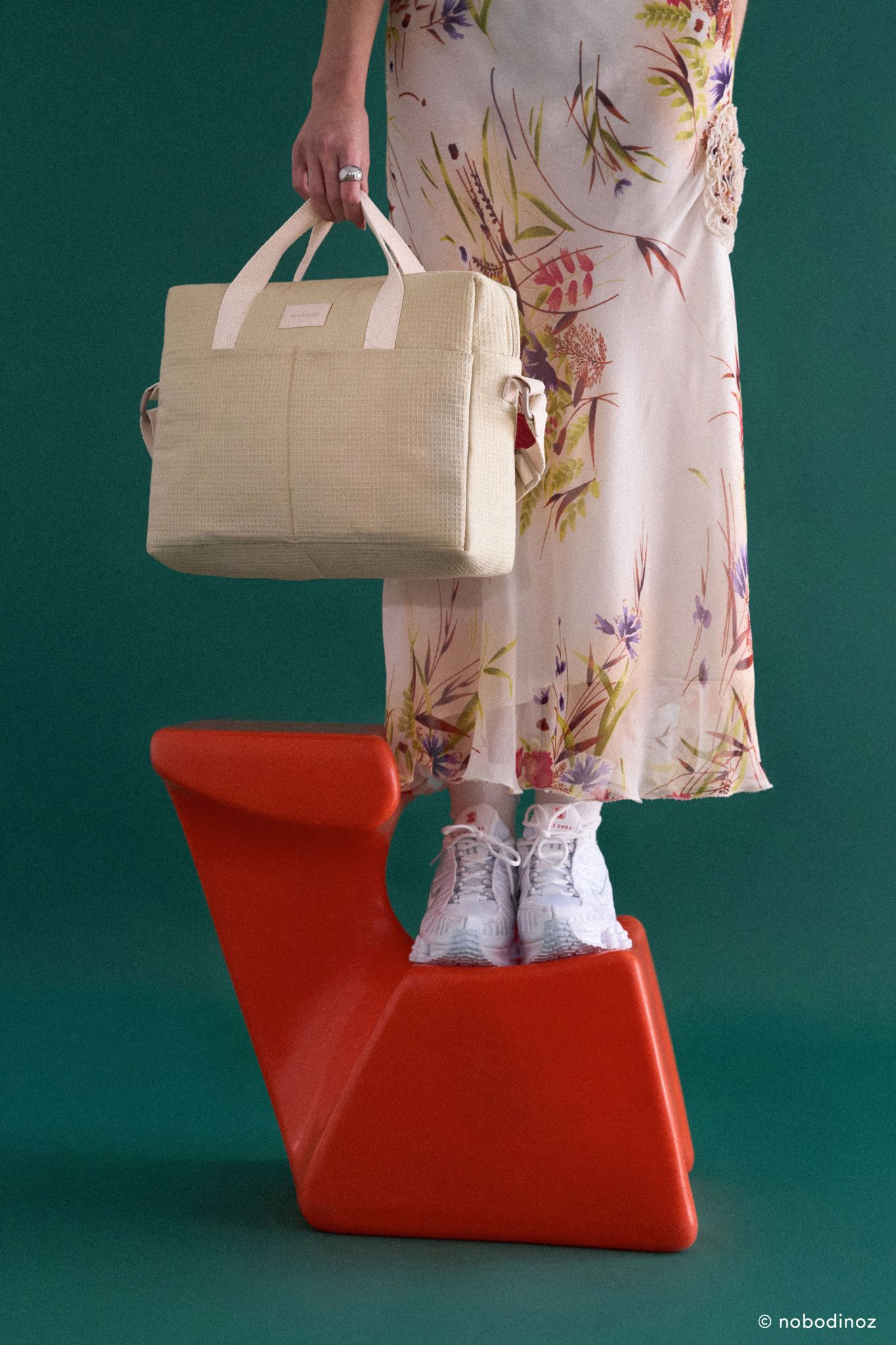 Sac à langer Nobodinoz vert d'eau Gala Opera tenu à la main par une femme en robe fleurie