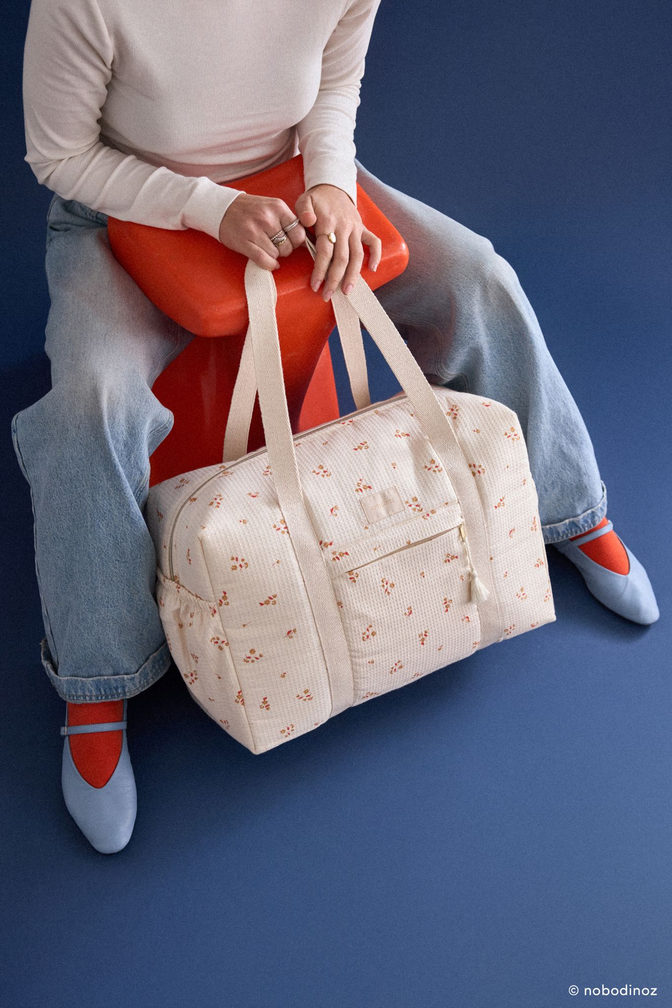 Sac à langer imperméable Opera yellow lily Nobodinoz porté par une personne assise