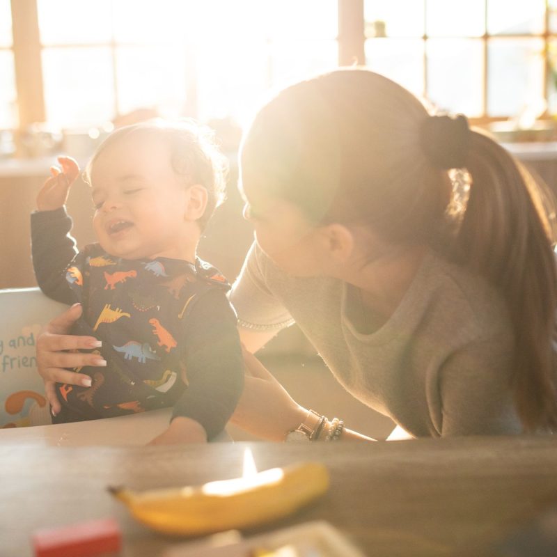 Babysitter tenant un bébé souriant dans sa chaise haute pendant le repas.