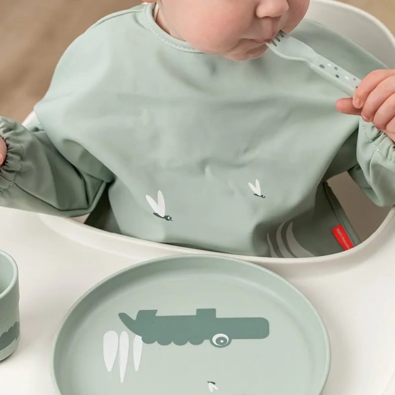 Enfant de 2 ans avec cuillère, bavoir et vaisselle adaptée pour le repas