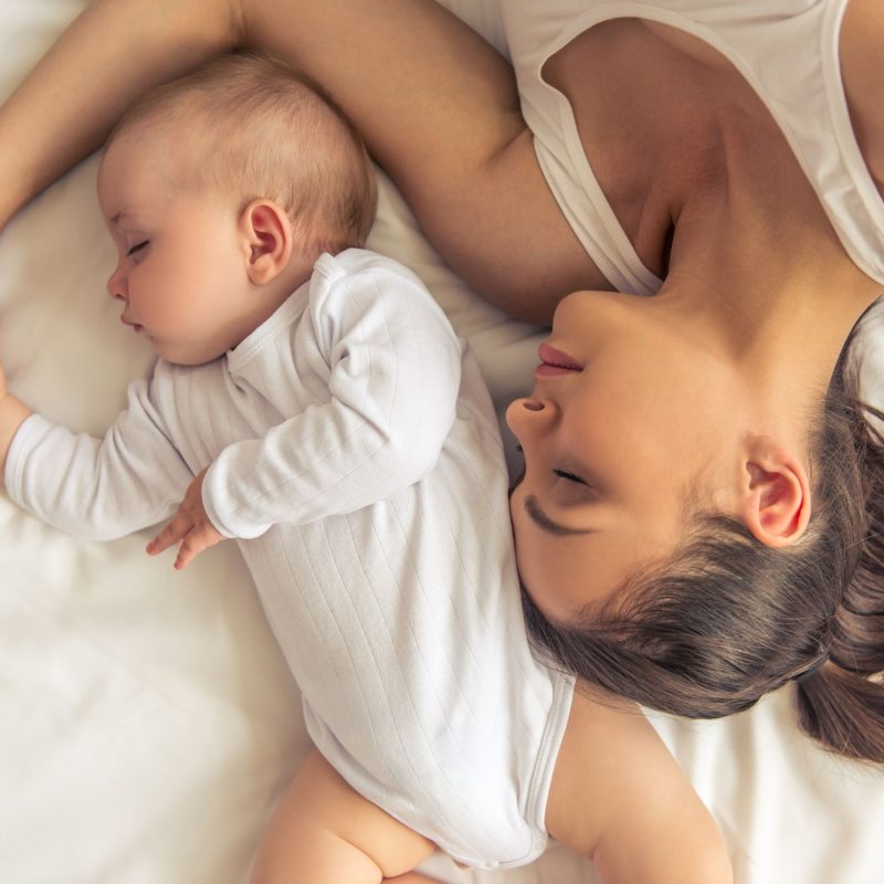 Maman allongée avec son bébé endormi, moment de repos post-partum avant la rééducation du périnée.