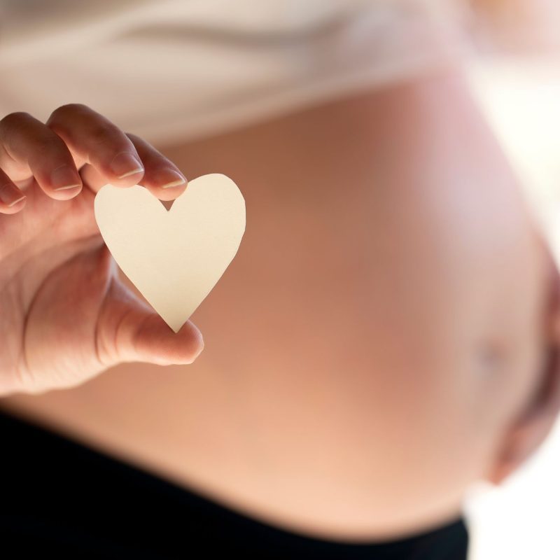 Femme enceinte tenant un cœur en papier, représentant la préparation de la liste de naissance à Montpellier.