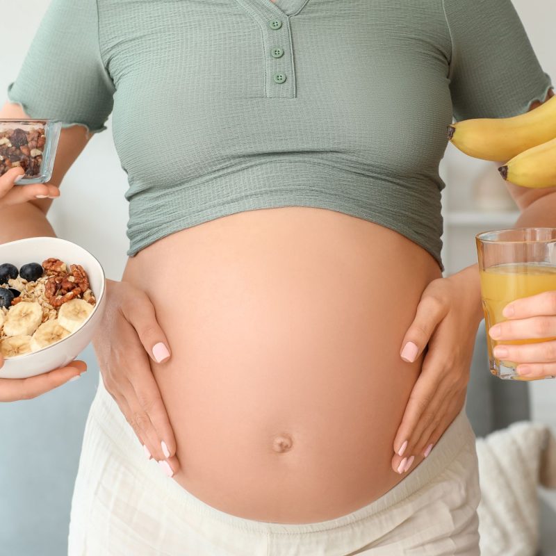 Femme enceinte recevant des aliments sains — fruits, noix et jus — symbolisant une alimentation équilibrée pendant la grossesse.