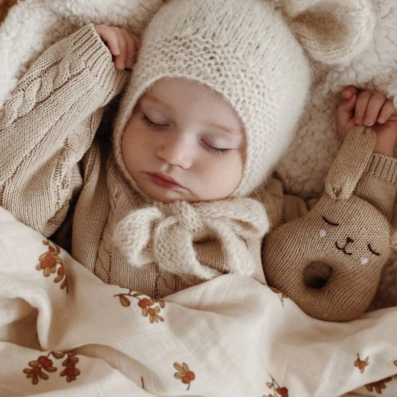 Bébé endormi avec bonnet en laine et peluche tricotée, apaisé par une berceuse bébé.