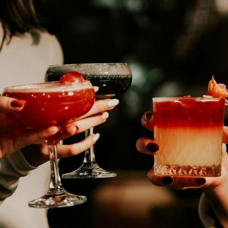 Mains tenant plusieurs verres de cocktails colorés sans alcool pendant une soirée, représentant des idées de cocktail sans alcool femme enceinte.