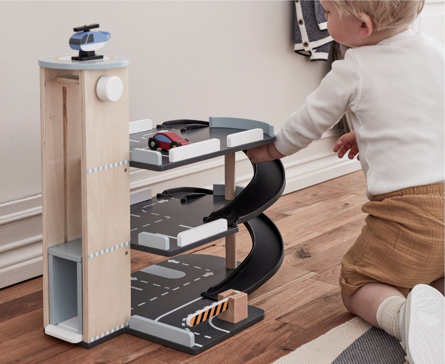 Enfant jouant avec un parking en bois Kid's Concept avec voitures et hélicoptère – idée cadeau Noël bébé et jouet d’imitation