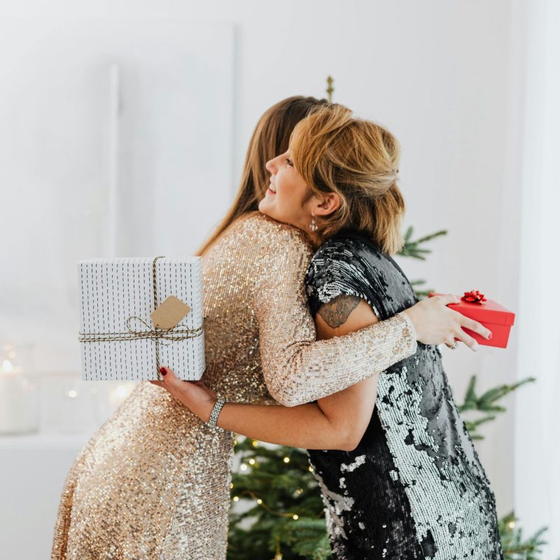 Deux femmes s’enlaçant et échangeant des cadeaux à Noël, illustrant un moment familial chaleureux avant un repas festif pour femme enceinte.
