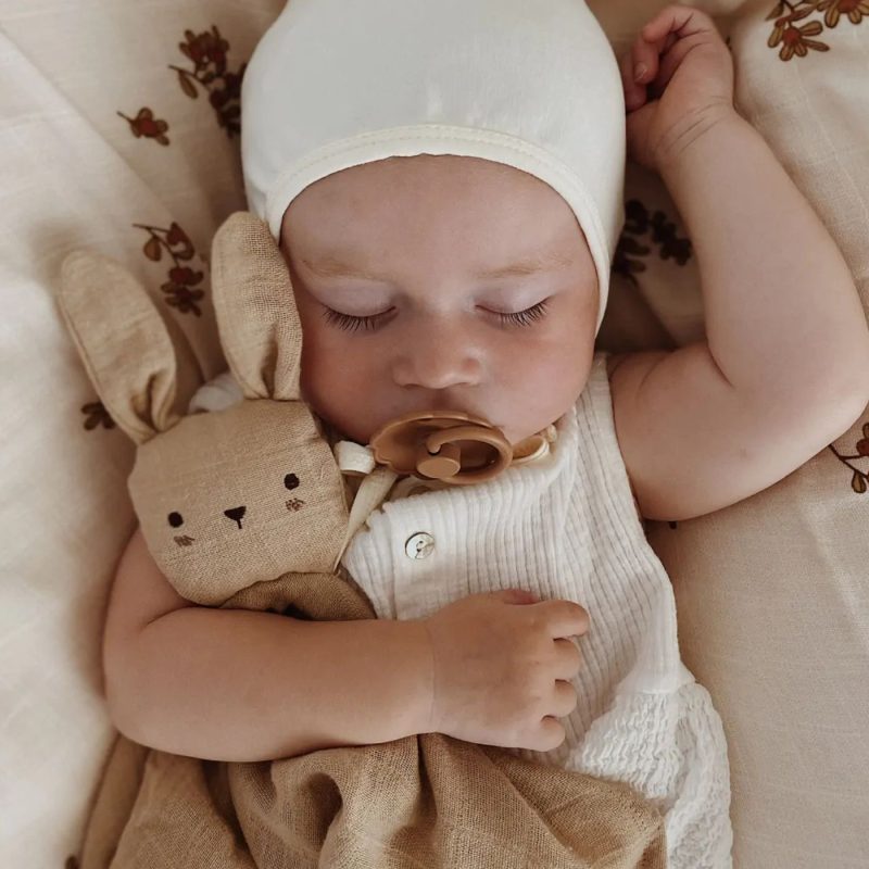 Bébé dormant avec une sucette et un doudous lapin beige contre lui