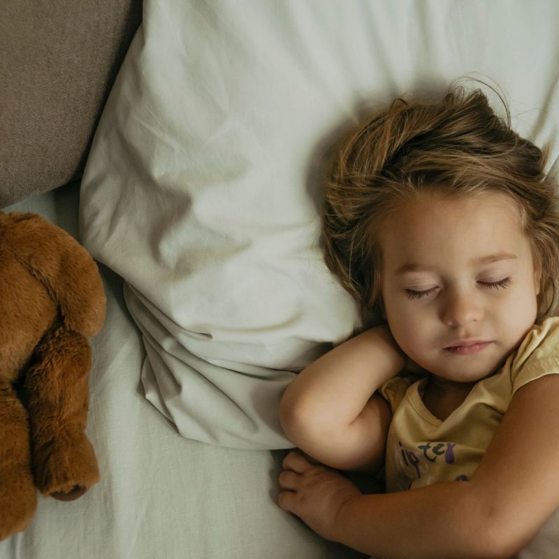 Enfant endormi près d’un ours en peluche, illustrant un sommeil serein après une terreur nocturne.