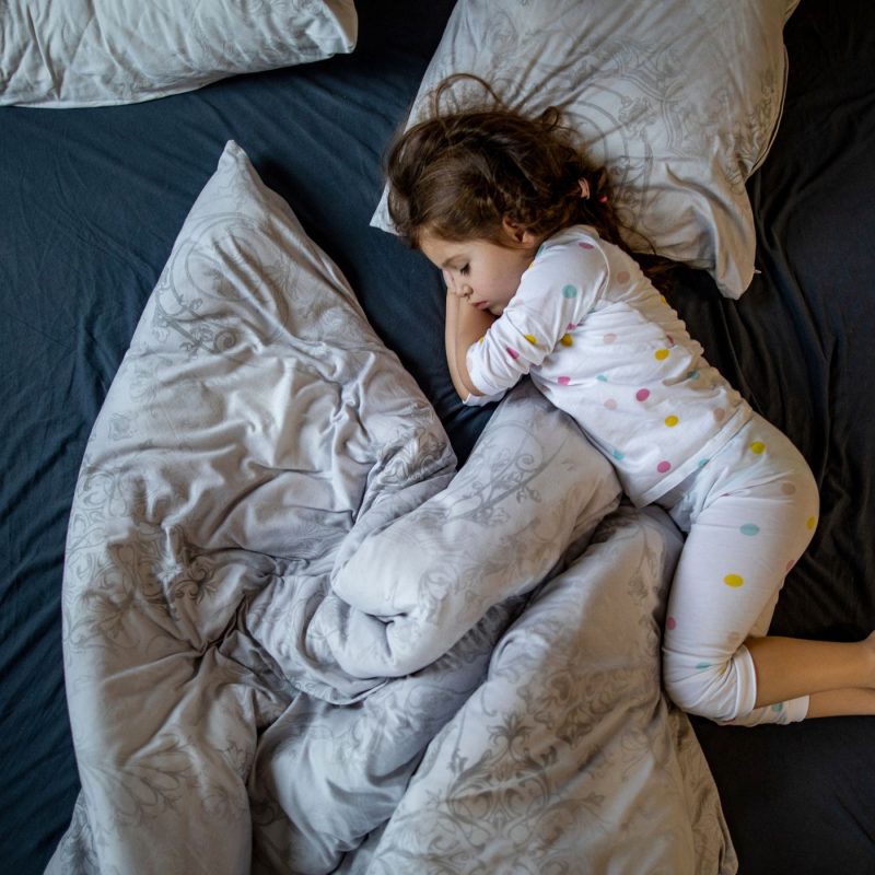Enfant dormant profondément dans un grand lit, représentant un sommeil calme après une terreur nocturne.