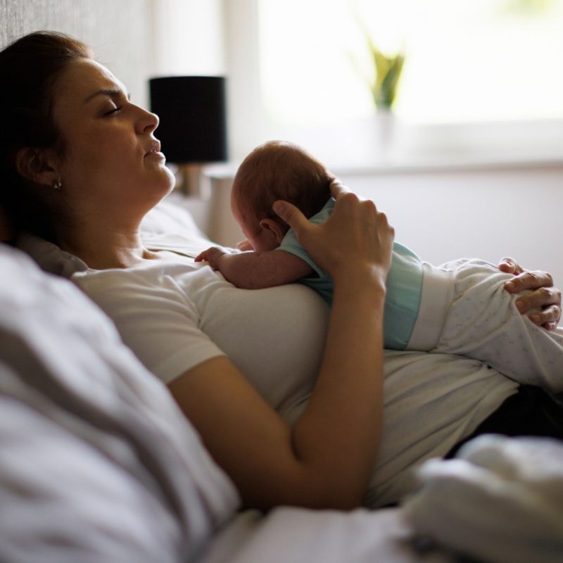 Maman allongée sur un lit avec son bébé sur la poitrine, illustrant la fatigue et la dépression post partum après l’accouchement.