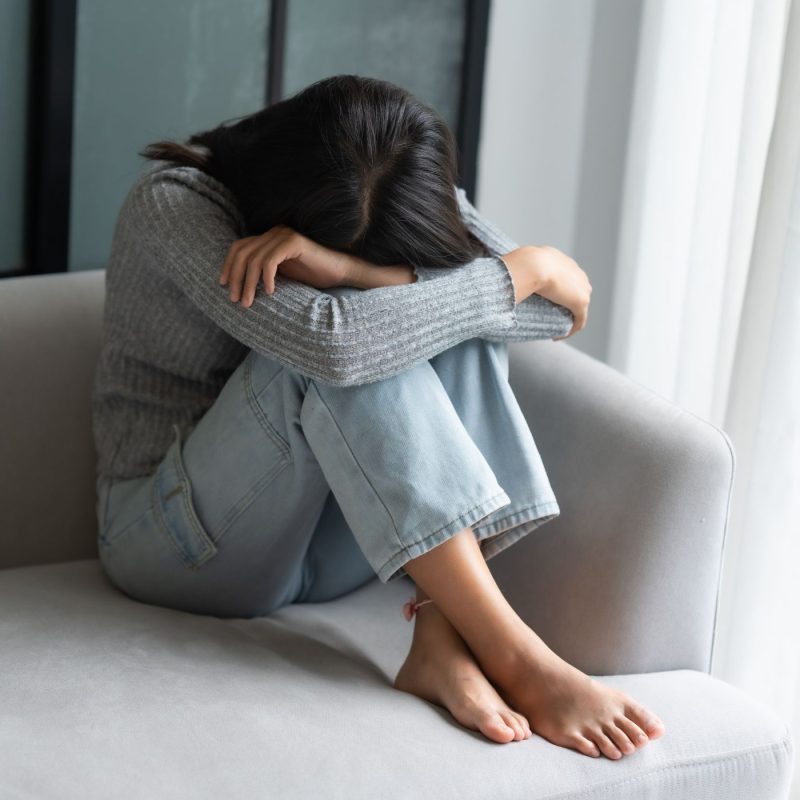 Maman assise sur un canapé, tête dans les bras, illustrant la dépression post-partum et l’épuisement après l’accouchement.