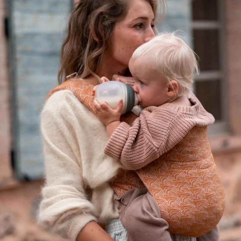 bébé boit un biberon dans les bras d’un parent quantité de lait bebe selon l’âge