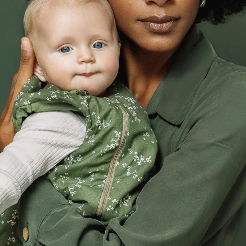 Bébé portant une gigoteuse verte dans les bras de sa maman pour illustrer comment habiller bébé nuit selon la température.