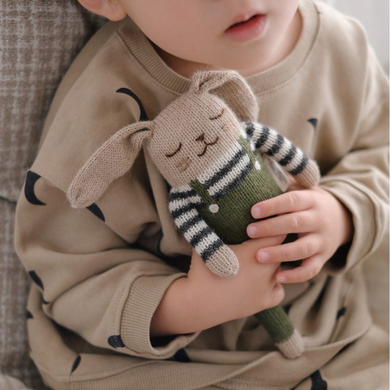 Main Sauvage doudou lapin salopette olive tenu par un bébé