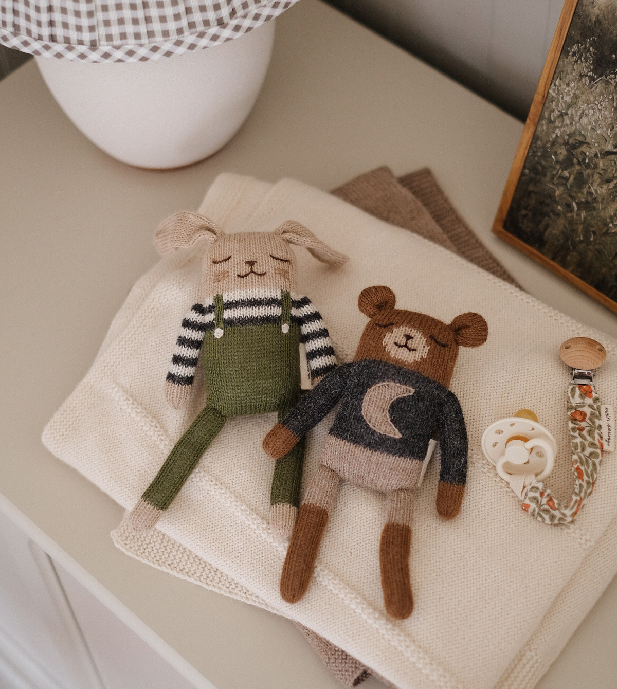 Main Sauvage doudou lapin en salopette olive posé sur un linge de bébé